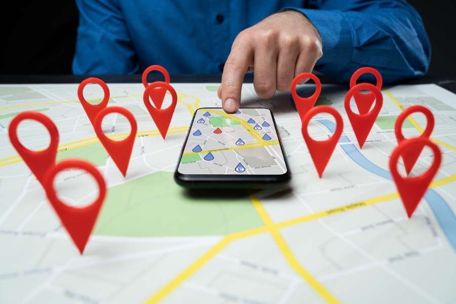 Hand pointing at smartphone with map and red location pins to master local SEO targeting