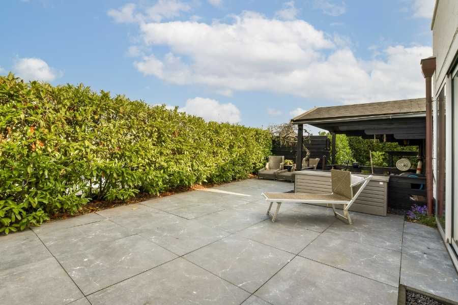 A modern outdoor patio with gray stone tiles and a sun lounger under a cloudy sky.