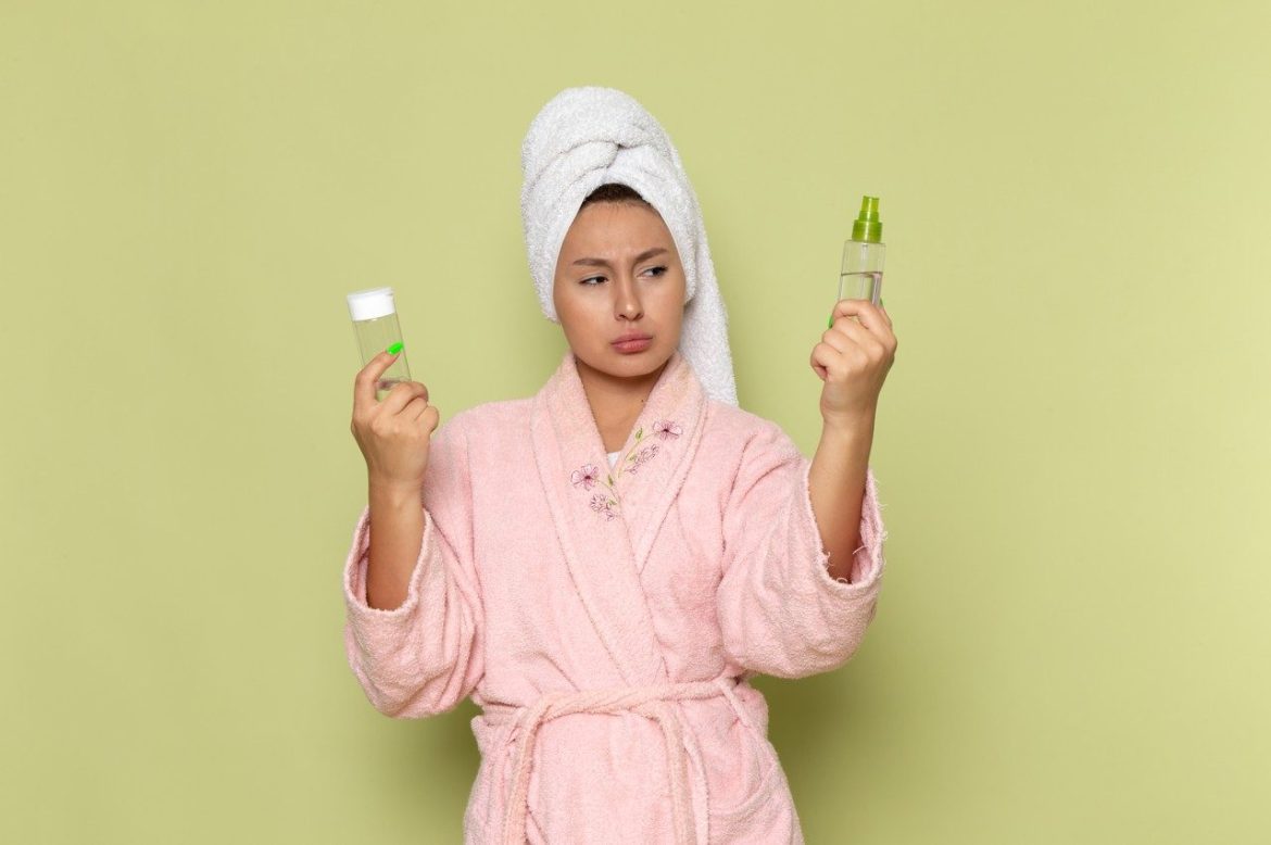A confused woman in a bath towel and bathrobe holding two skincare bottles, highlighting the counterfeit skincare problem.